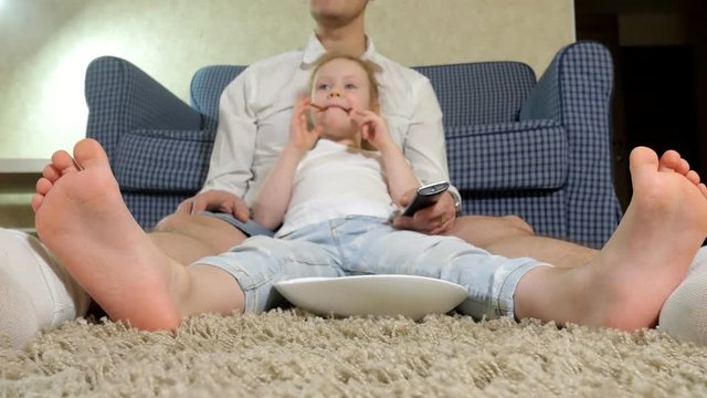 man and daughter watching television, sitting on the floor eating snacks