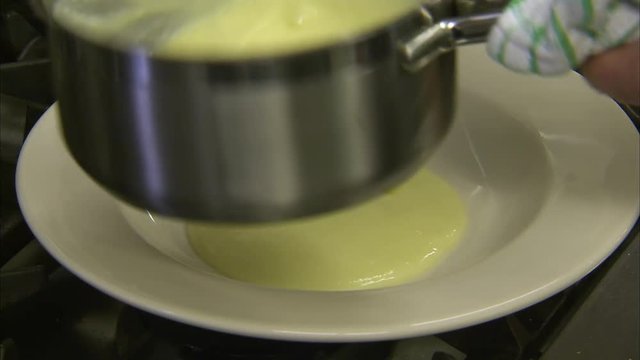 Plating a dish on a white round plate. The fried monkfish meat is placed on a beautiful white cream and stripped vegetables. The shot is steady and taken in medium.