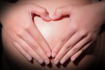 Obraz na płótnie Canvas woman holding her hands in a heart shape on her baby bump pregnant belly with fingers on black background