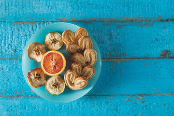 cookies in the shape of a heart with decorative slices of dried apples on blue wooden surface with space for text