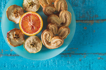cookies in the shape of a heart with decorative slices of dried apples on blue wooden surface with space for text