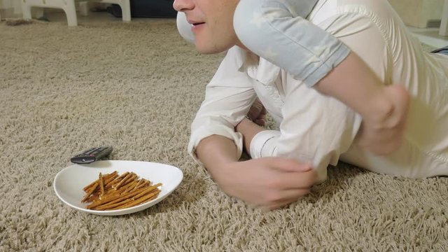 man and daughter watching television, sitting on the floor eating snacks