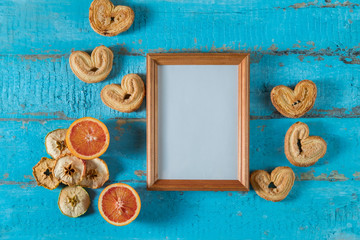 wooden photo frame on blue wooden surface texture with empty place for text or image with slices of dried apple, red orange