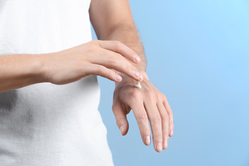 Man applying body cream on color background, closeup
