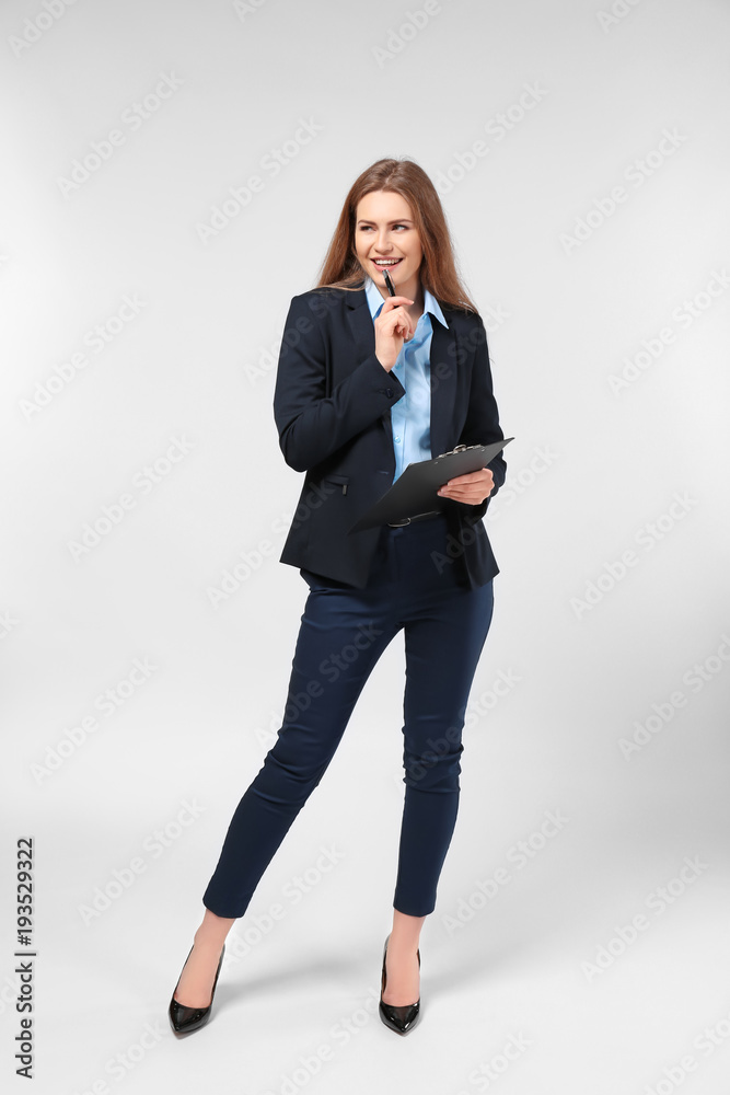 Wall mural Beautiful young woman in elegant suit and with clipboard on light background