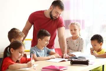 Male teacher helping children with homework in classroom at school