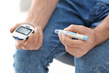 Diabetic man holding digital glucometer and lancet pen, closeup