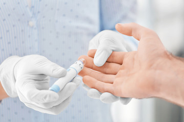 Doctor taking sample of diabetic patient's blood using lancet pen, closeup
