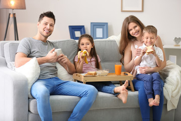 Happy family having breakfast on sofa at home