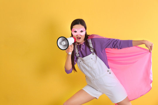 Young woman in superhero costume with megaphone on color background