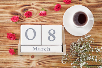 Block calendar, cup of coffee and flowers on wooden background. International Women's Day celebration