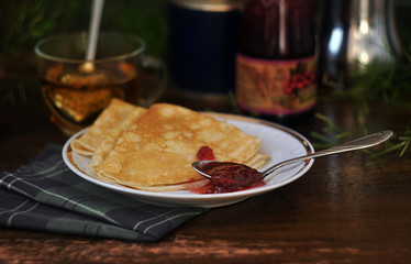 Pancakes with berry jam in a plate on a wooden table and kitchen utensils in the background. Close-up.