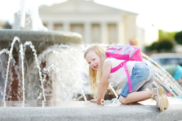 Cute little girl playing by city fountain on hot and sunny summer day. Child having fun with water in summer.