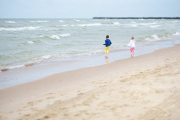 Two little sisters having fun on a sandy beach on warm and sunny summer day. Kids playing by the ocean.