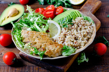 Healthy salad bowl with quinoa, tomatoes, chicken, avocado, lime and mixed greens, lettuce, parsley on wooden background close up. Food and health.