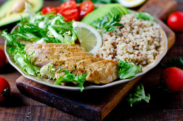 Healthy salad bowl with quinoa, tomatoes, chicken, avocado, lime and mixed greens, lettuce, parsley on wooden background close up. Food and health.