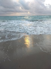 turquoise colored sea and golden light reflections in sand at dawn on the coast