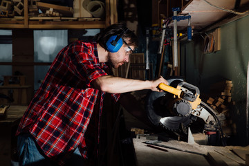 Obraz na płótnie Canvas brunette man profession carpenter builder saws with a circular saw a wooden board.