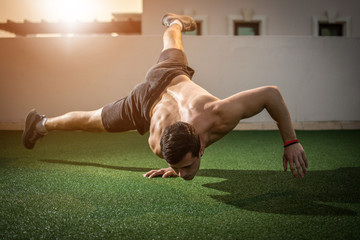 Young athletic man balancing while doing a one hand push up and holding his body in the air...