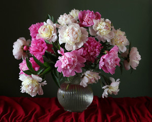 Bouquet of peonies in a jug on a table with a red tablecloth.