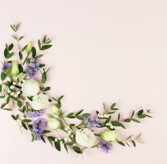 Flowers background. Frame wreath of green eucalyptus branches and white and purple flowers on pale pink background. top view. copy space. Holidays background