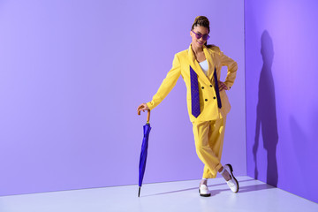 african american girl posing in fashionable yellow suit with purple umbrella, on trendy ultra violet background