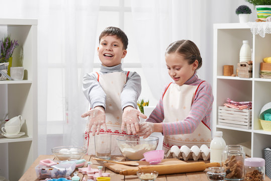Girl and boy cooking in home kitchen. Children show hands with flour.
