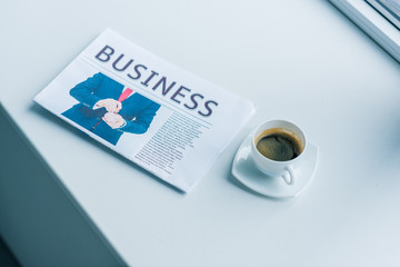 close up view of cup of coffee and business newspaper on white surface