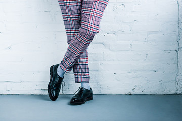 cropped shot of man in stylish pants and shoes standing against white brick wall