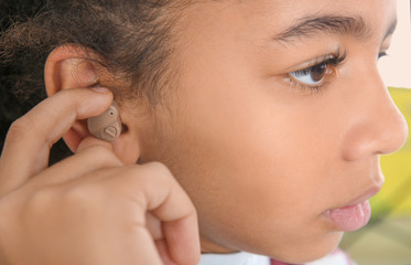 Little girl putting hearing aid in ear, closeup