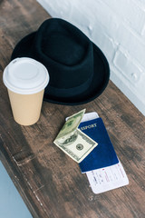 close up view of arranged passport, cash, coffee to go and hat on wooden bench