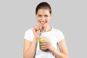 Beautiful young woman drinking lemonade on grey background
