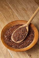 Wooden spoon with flax seeds in a plate on rustic background, top view, close-up, shallow depth of field, vertical