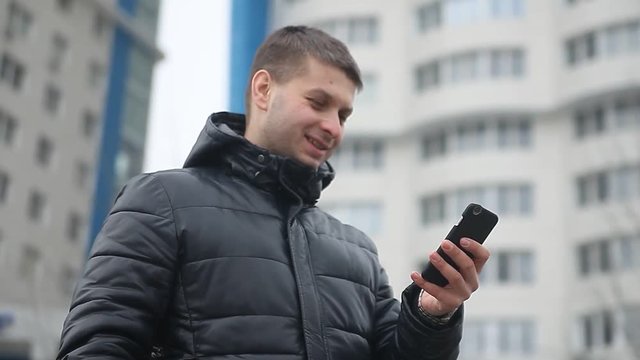 the man is talking on the phone smartphone. man in winter in a winter jacket speaks on a outdoors skyscraper smartphone