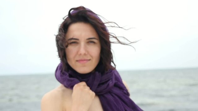 A closeup of a glamour young woman who stands on a sea coast. She has a violet pareo on her head in summer in slo-mo. The wind flutters her hair