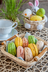 multicolored meringues macaroons in a wicker basket with white Cup and Easter eggs