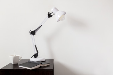 The white lamp on the bedside next to a book and a cup of tea