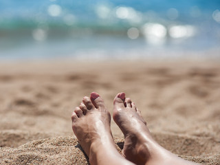 Female feet with manicured nails on the beach against the sea.