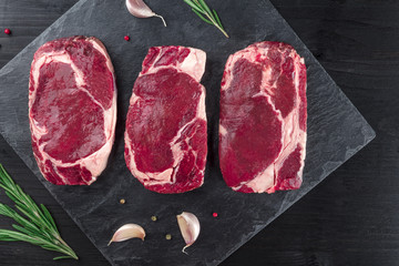 Three slices of raw meat on black with seasoning and copyspace