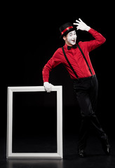 happy mime leaning on frame and waving hand isolated on black