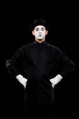 mime standing with hands akimbo and looking at camera isolated on black