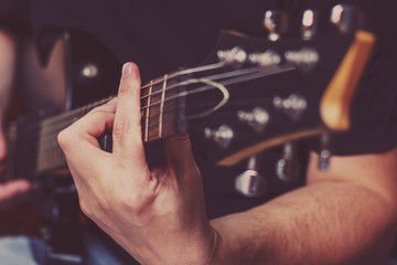 Fototapeta premium Closeup of hands of a guy playing electrical guitar on a black background ,with only his fingers in focus