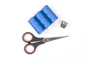 Blue sewing threads with black scissors and metal thimble on a white background