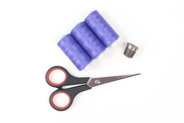 Purple sewing threads with black scissors and metal thimble on a white background