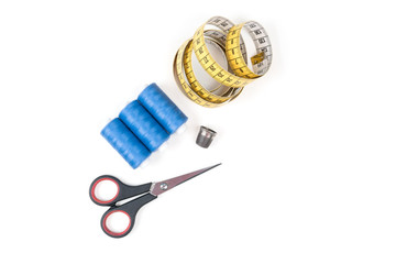 Sewing supplies and tools, three blue sewing threads, yellow measuring tape with black numbers, small closed scissors and metal thimble on a white background