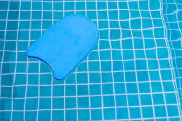 A blue swimming board floating on the pool water. Copy space.