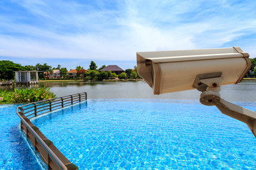 CCTV security camera secure to protect and outdoor swimming pool and lake with beautiful sky. Copy space.