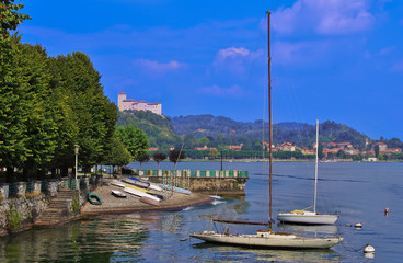lakefront of Arona on Lake Maggiore,Italy, with moored boats and view on Angera Castle in a beautiful summer day