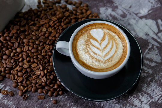 Top view of coffee cup with latte art and beans on old vintage table.