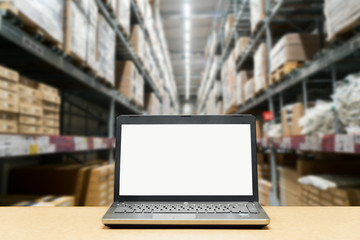 Laptop with white blank screen on brown wooden desk and blurred warehouse store background. - Powered by Adobe